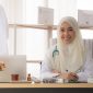 Portrait of charming muslim female doctor working at office desk and smiling at camera