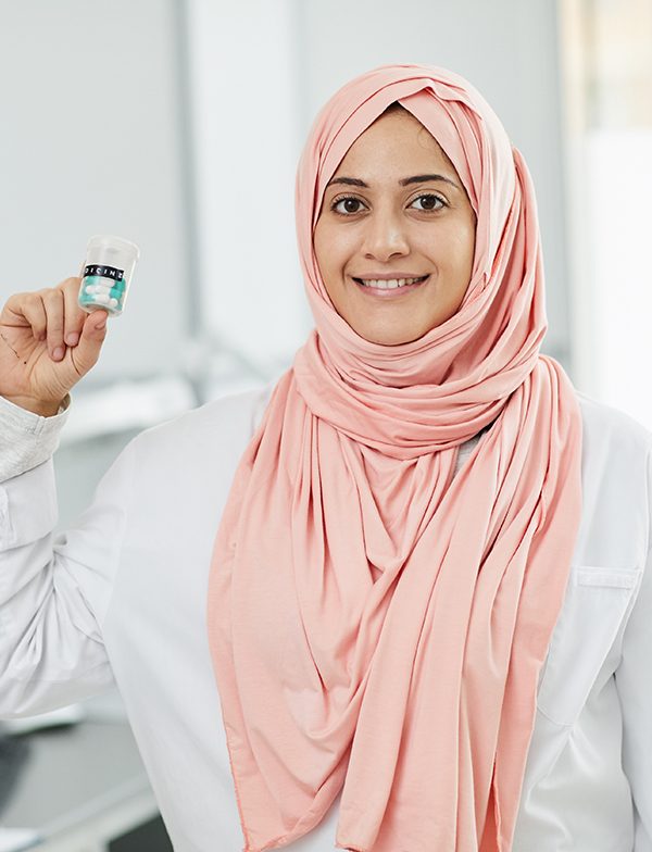 Waist up portrait of young Middle-Eastern woman working as nurse in medical clinic and smiling at camera holding bottle of pills, copy space